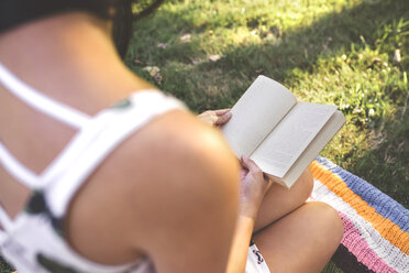 Nahaufnahme einer Frau, die auf einer Decke sitzt und ein Buch liest - DAPF00379