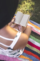 Nahaufnahme einer Frau, die auf einer Decke sitzt und ein Buch liest - DAPF00380