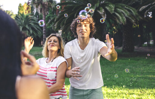 Junge glückliche Freunde haben Spaß und spielen mit Seifenblasen im Park - DAPF00386