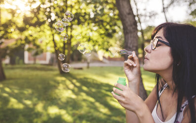 Young woman blowing soap bubbles in park - DAPF00387