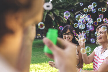 Junge glückliche Freunde haben Spaß und spielen mit Seifenblasen im Park - DAPF00389