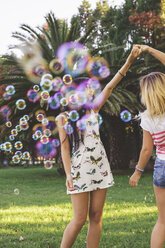 Female friends having fun with soap bubbles in park - DAPF00391