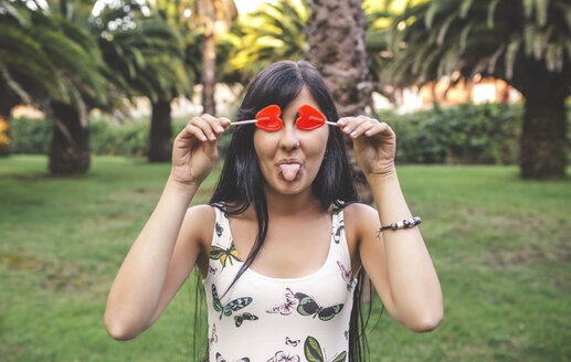 Playful young woman covering her eyes with heart-shaped lollipop - DAPF00398