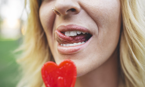 Nahaufnahme einer jungen Frau, die einen herzförmigen Lutscher leckt, lizenzfreies Stockfoto