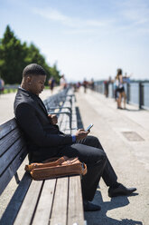 Businessman sitting on bench looking at cell phone - GIOF01486