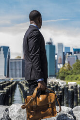 USA, Brooklyn, Geschäftsmann mit Aktentasche vor der Skyline von Manhattan - GIOF01499