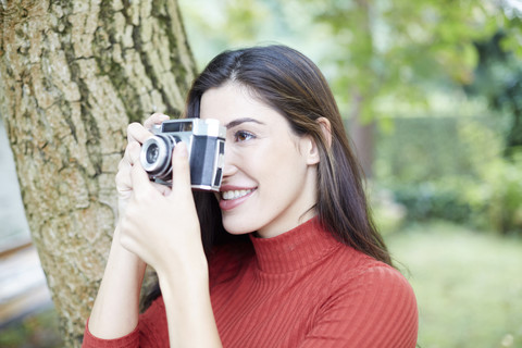 Smiling woman taking pictures with vintage camera in the garden stock photo