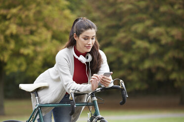 Woman with bicycle in an autumnal park text messaging - FMKF03111