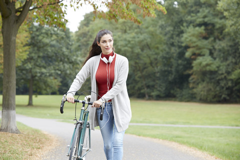 Woman with headphones and bicycle in an autumnal park stock photo