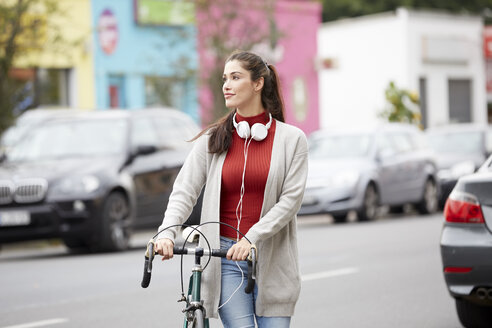 Entspannte Frau mit Kopfhörern und Fahrrad beim Überqueren der Straße - FMKF03116