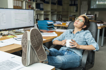 Woman sitting in office with feet up, taking a break - TCF05164