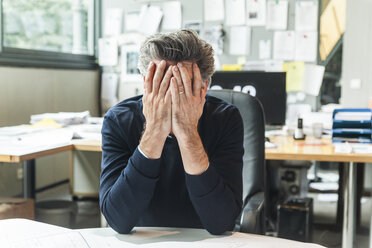 Reifer Mann sitzt im Büro mit Kopf in den Händen - TCF05168