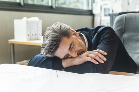 Überarbeiteter Architekt schläft am Schreibtisch, lizenzfreies Stockfoto