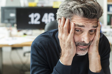 Reifer Mann sitzt im Büro mit Kopf in den Händen - TCF05171