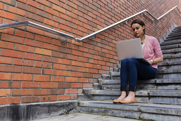 Frau sitzt auf einer Treppe und arbeitet mit einem Laptop - BOYF00596