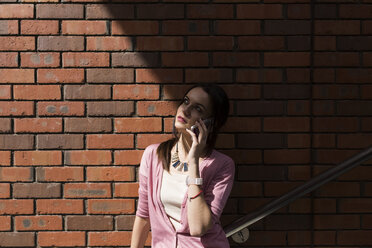 Junge Frau am Telefon vor einer Backsteinmauer - BOYF00600