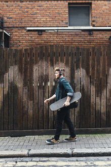 Junger Skateboarder, der auf dem Bürgersteig läuft und mit Kopfhörern Musik hört - BOYF00606