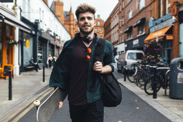 Ireland, Dublin, portrait of young man with skateboard walking on the street - BOYF00616