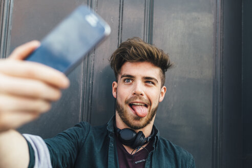 Porträt eines jungen Mannes, der ein lustiges Gesicht zieht und ein Selfie mit seinem Smartphone macht - BOYF00625