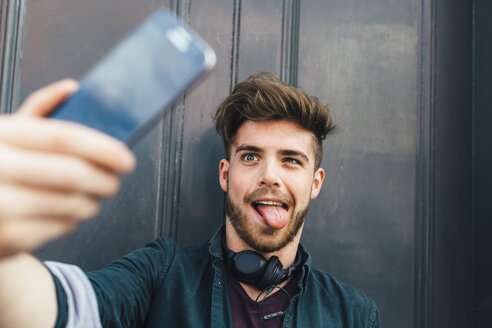 Portrait of young man pulling funny face taking selfie with smartphone - BOYF00625