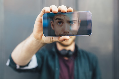 Display eines Smartphones zeigt einen jungen Mann, der ein lustiges Gesicht zieht, lizenzfreies Stockfoto