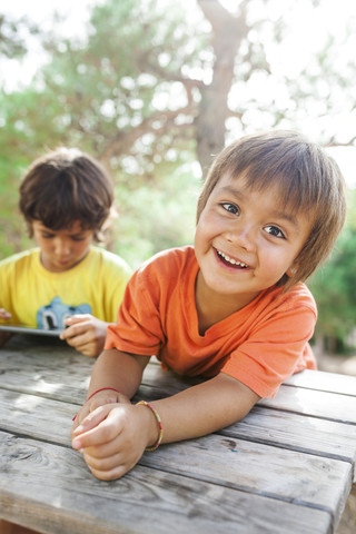 Porträt eines entspannten kleinen Jungen mit seinem Bruder, der ein Tablet im Hintergrund benutzt, lizenzfreies Stockfoto
