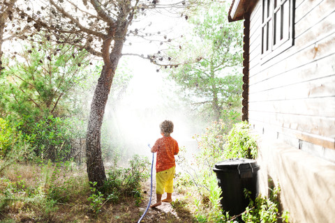 Rückansicht eines kleinen Jungen, der mit einem Gartenschlauch spielt, lizenzfreies Stockfoto