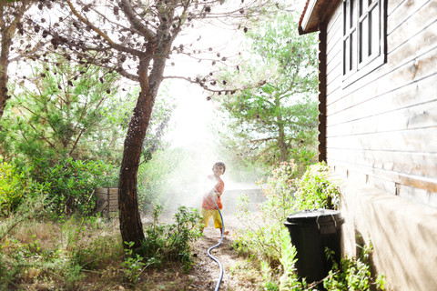 Kleiner Junge spielt mit Gartenschlauch, lizenzfreies Stockfoto