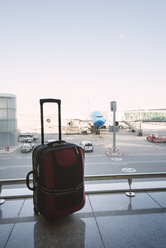 Red suitcase at airport, airplane in background - RAEF01515