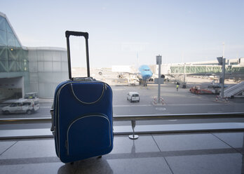 Blue suitcase at airport, airplane in background - RAEF01516