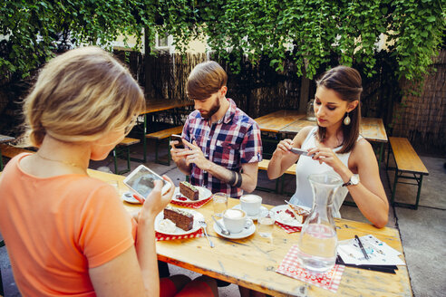Friends sitting outdoors with coffee and cake taking cell phone pictures - AIF00378