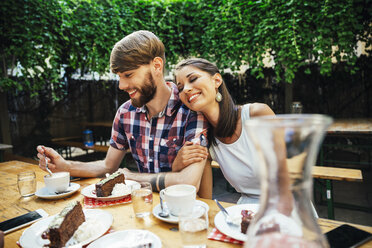 Glückliches junges Paar sitzt im Freien bei Kaffee und Kuchen - AIF00383