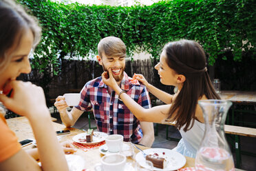 Glückliches junges Paar mit Freundin sitzt im Freien bei Kaffee und Kuchen - AIF00391