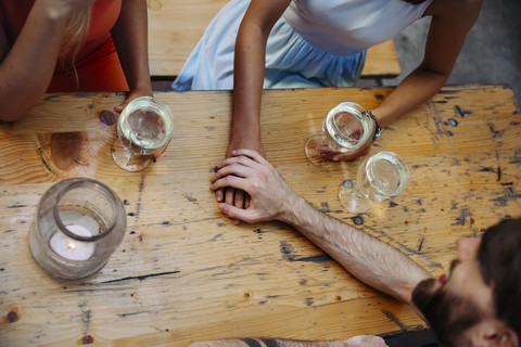Junges Paar Hand in Hand und Freund trinken Schorle in einer Kneipe im Freien, lizenzfreies Stockfoto