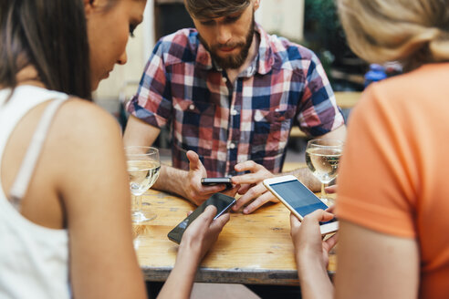 Friends using cell phones and drinking spritzer at outdoor pub - AIF00405