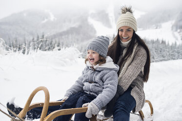 Glückliche Mutter mit Tochter auf Schlitten in Winterlandschaft - HAPF00949