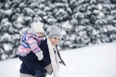 Happy mother carrying daughter piggyback in winter landscape - HAPF00987