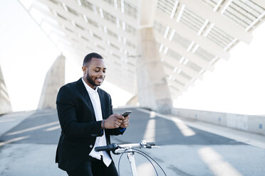 Smiling businessman on bicycle looking at cell phone - JRFF00947