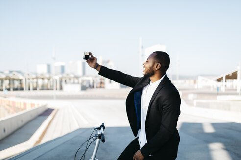 Lächelnder Geschäftsmann mit Fahrrad, der ein Selfie macht - JRFF00949