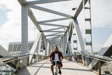 Lächelnder Mann fährt Fahrrad auf einer Brücke - JRFF00971