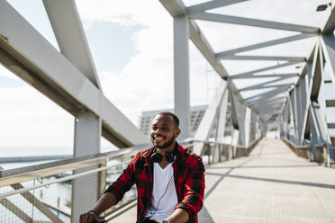 Smiling man riding bicycle on a bridge - JRFF00972