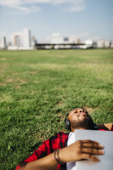 Man lying in grass with laptop listening to music - JRFF00974