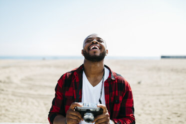 Laughing man holding an old-fashioned camera near the beach - JRFF00981