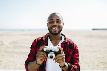 Lächelnder Mann mit einer altmodischen Kamera in der Nähe des Strandes - JRFF00982