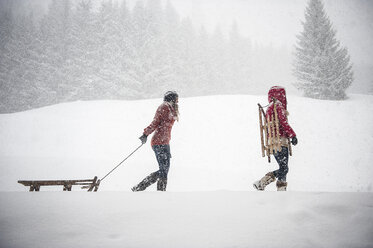 Zwei junge Frauen mit Schlitten bei starkem Schneefall - HHF05411