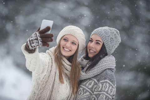 Zwei junge Frauen machen ein Selfie im Schneefall, lizenzfreies Stockfoto