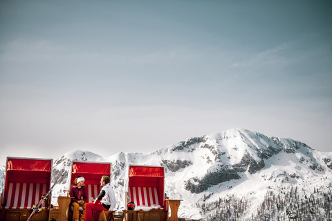 Österreich, Altenmarkt-Zauchensee, Paar im Strandkorb mit Kapuze in den Bergen, lizenzfreies Stockfoto