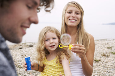 Eltern mit Tochter an einem See, die Seifenblasen blasen - FSF00580