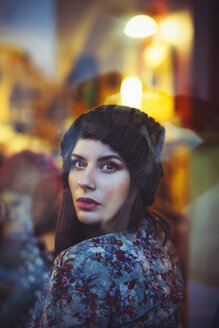 Porträt einer jungen Frau, die durch das Fenster einer Kneipe am Abend starrt - LCUF00060