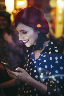 Smiling young woman wearing red hat behind windowpane of a pub in the evening - LCUF00064